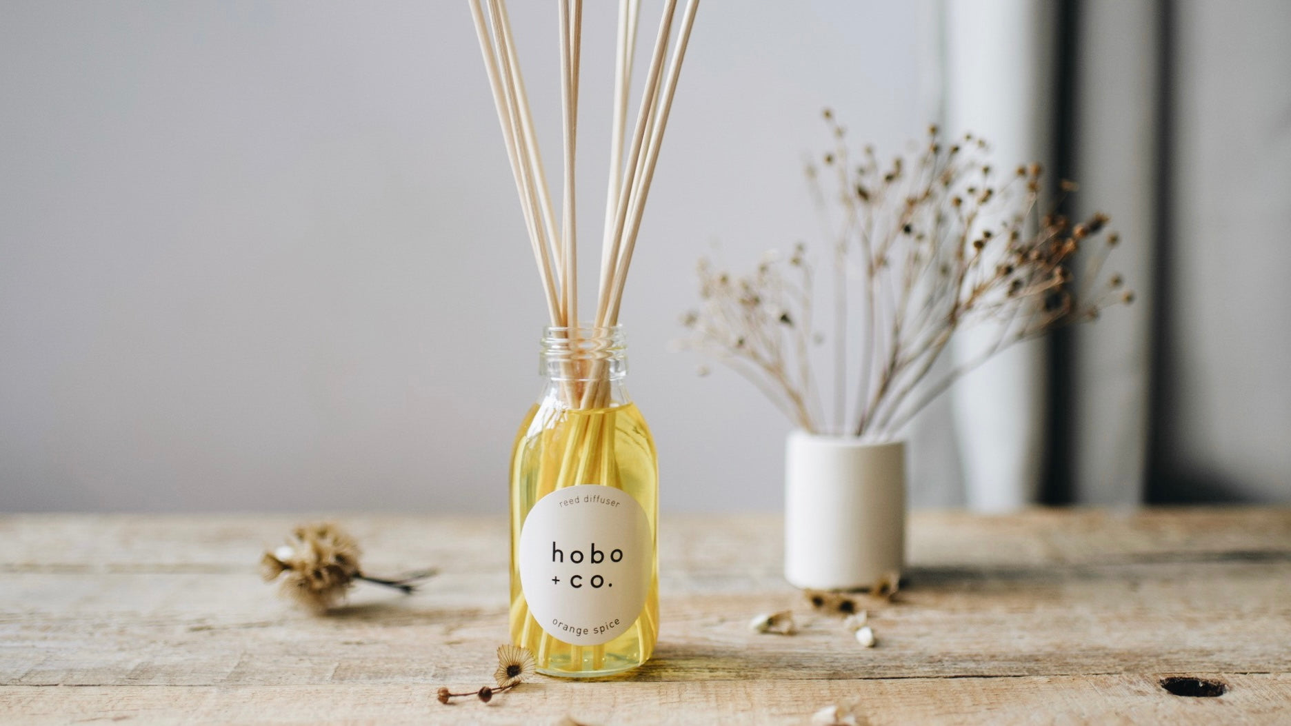 hobo + co reed diffuser labeled orange spice on a wooden surface with wintery decorative elements.
