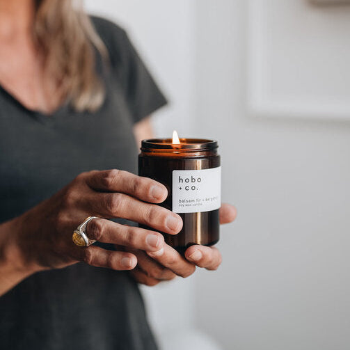 Person holding a lit candle with 'hobo & co.' label against a neutral background