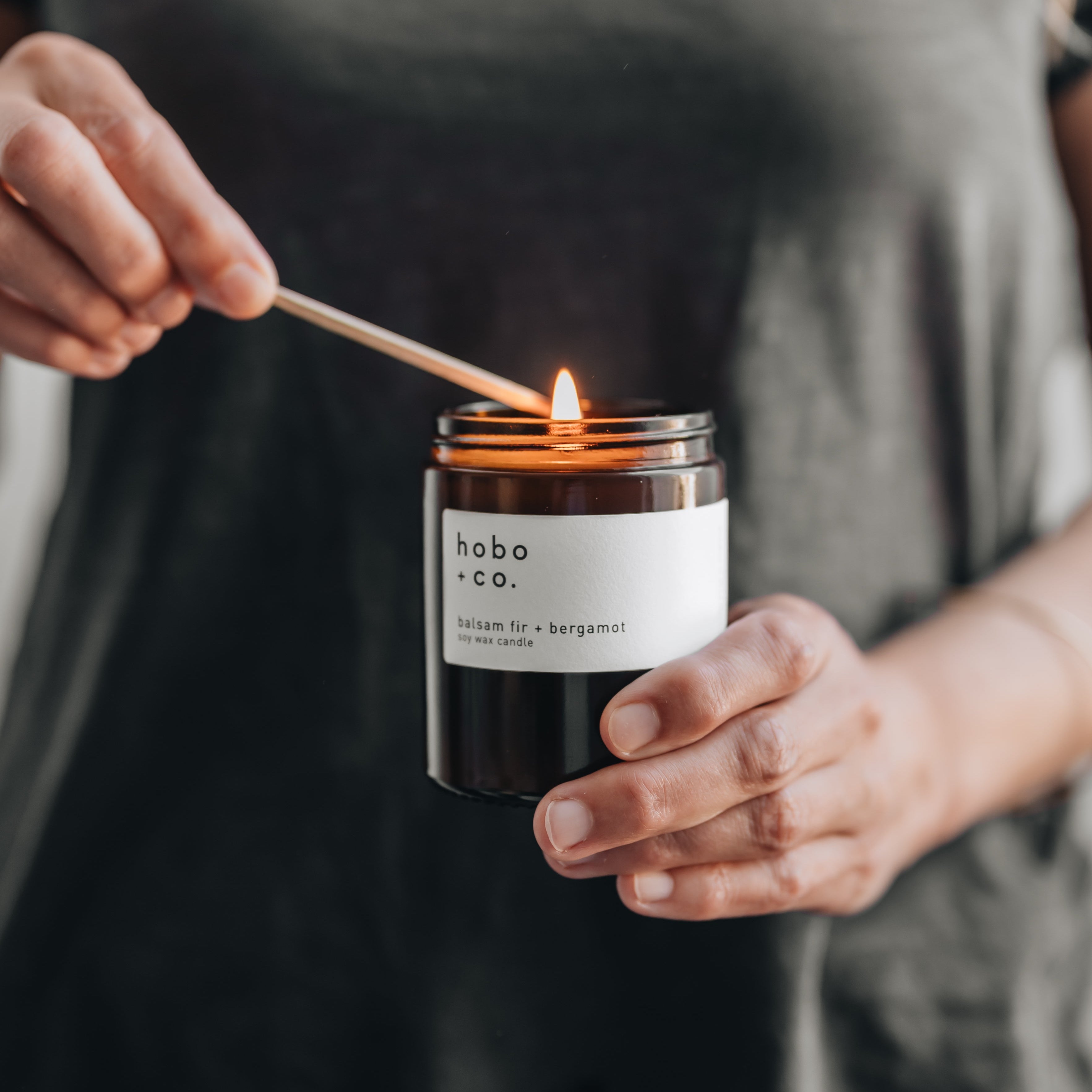 Person lighting a candle labeled 'hobo & co.'