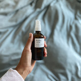 Hand holding a room mist bottle labeled 'hoba & co' against a soft, blurred background