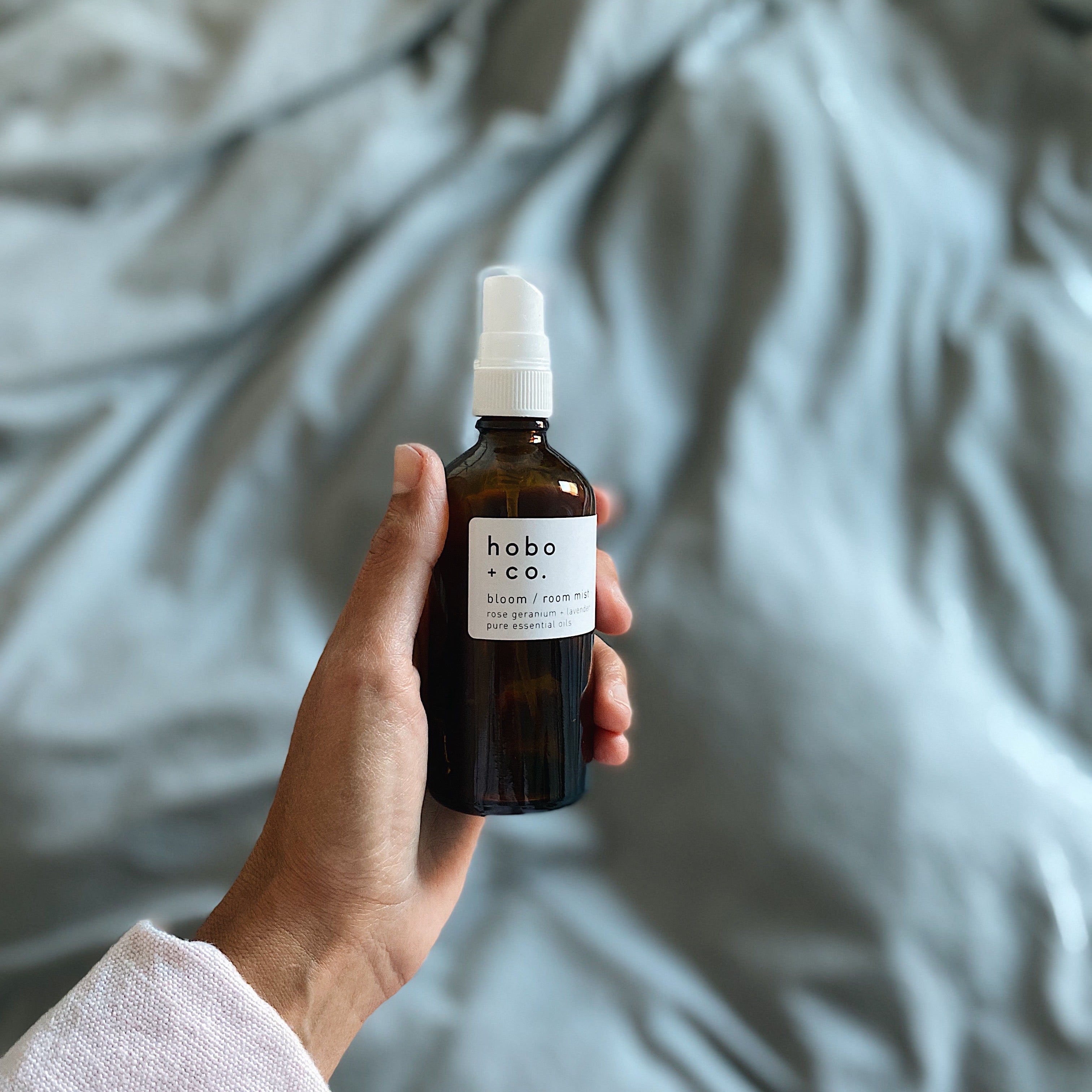 Hand holding a room mist bottle labeled 'hoba & co' against a soft, blurred background