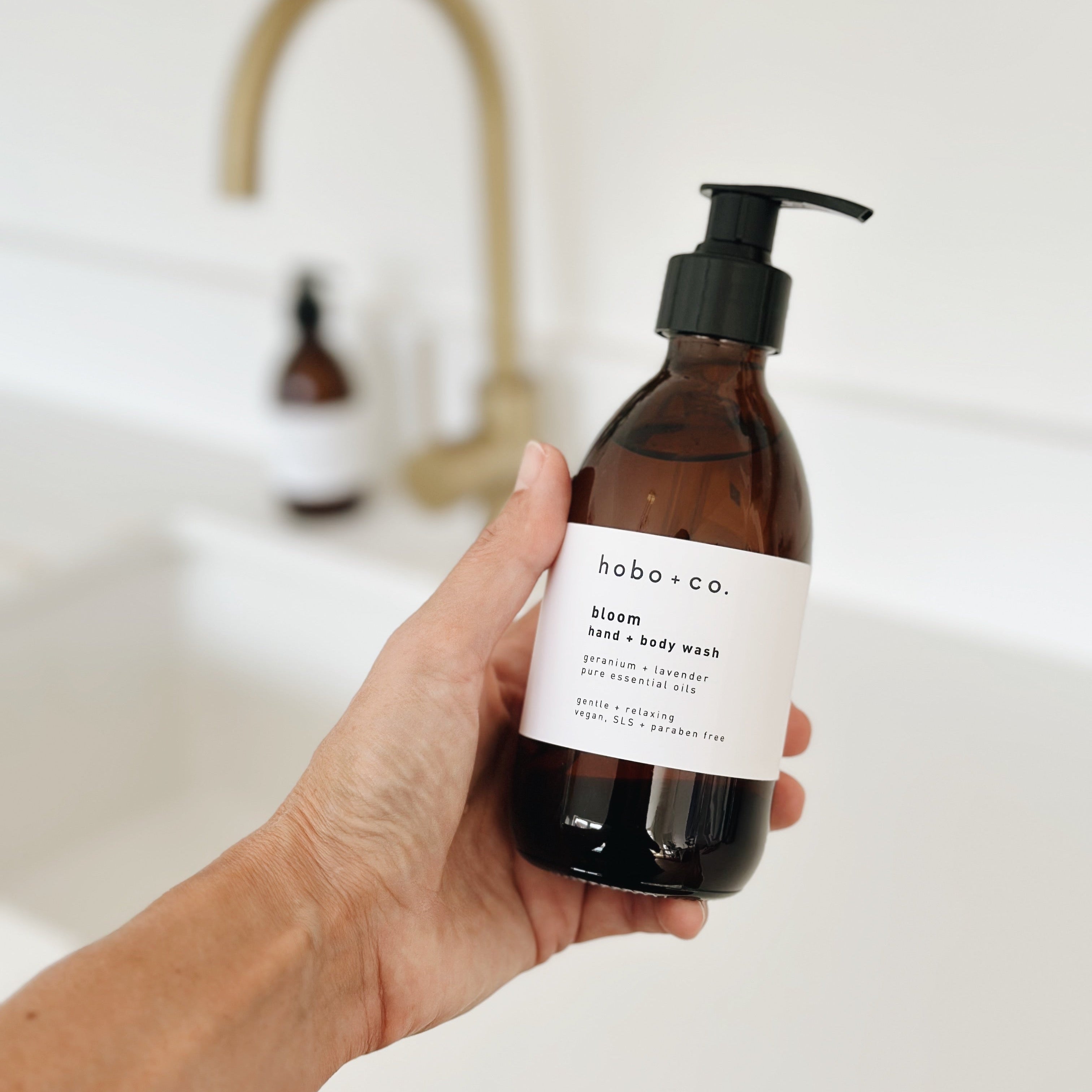 A hand holding a brown amber glass pump bottle of hobo + co.