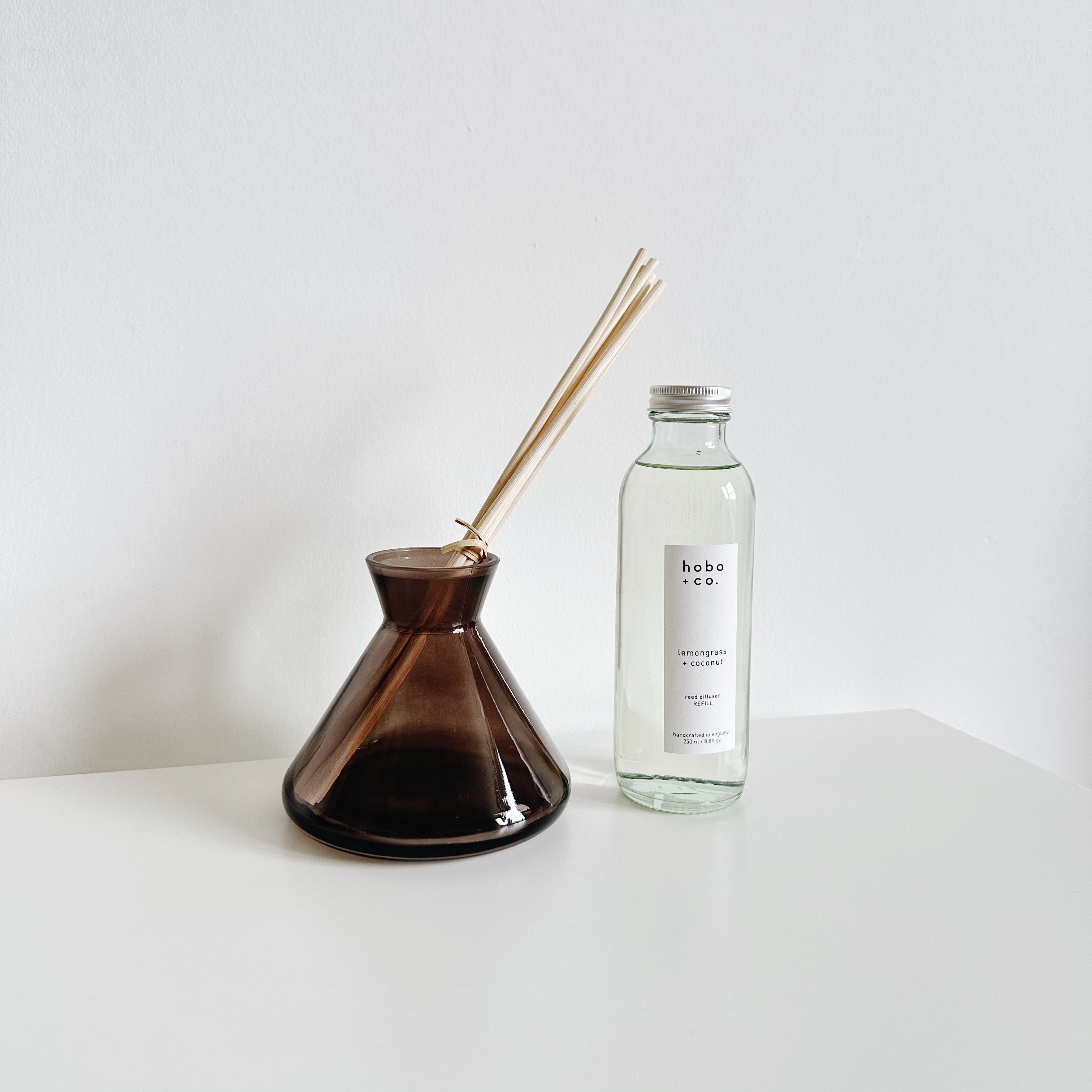 modern large smoky grey reed diffuser vessel with a clear diffuser refill bottle next to it on white background