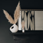 reed diffuser on a black fireplace with a mirror in the background with a cream vase and pampas grass