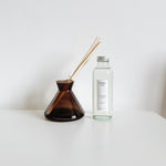 Modern diffuser vessel and clear refill bottle on a white surface with a white background