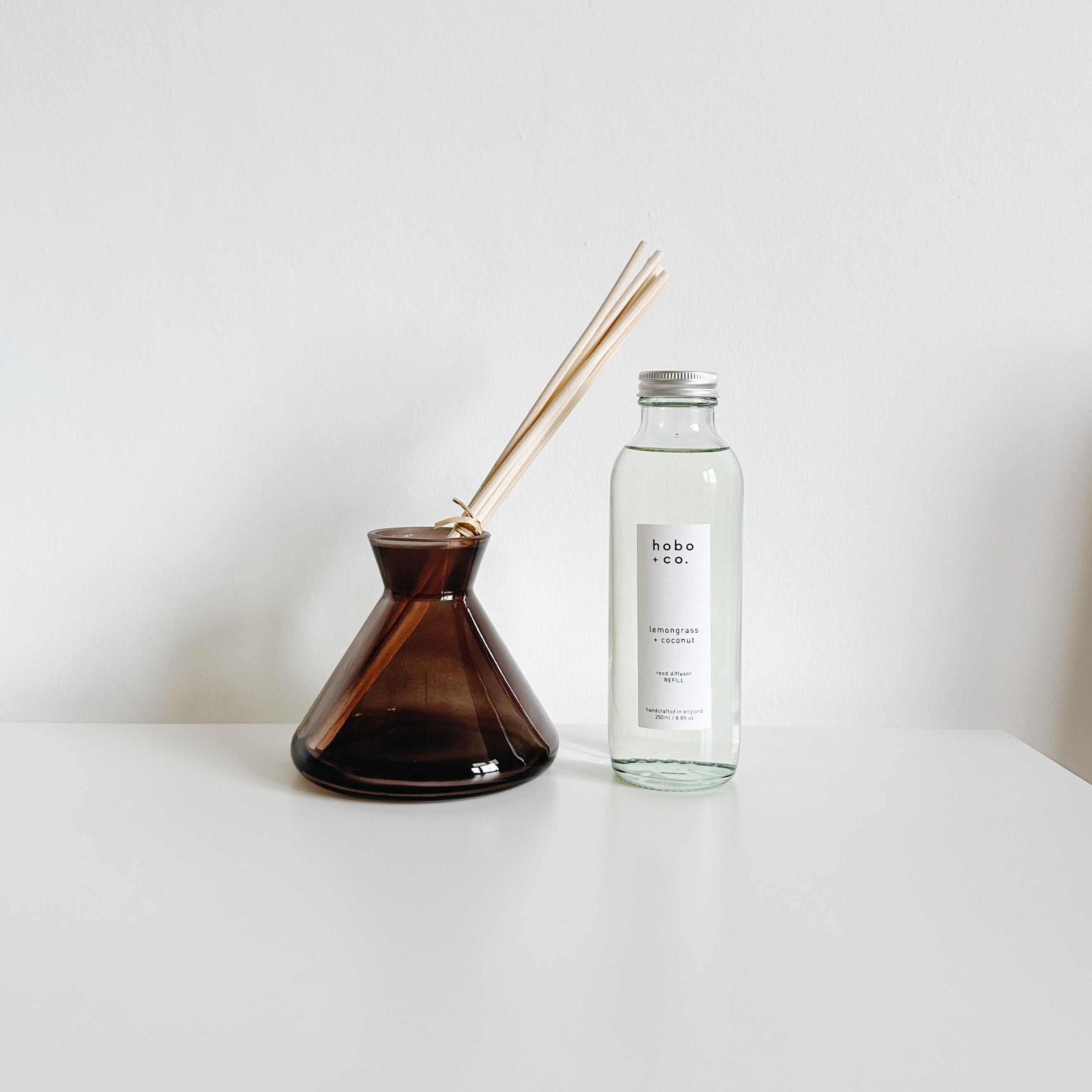 Modern diffuser vessel and clear refill bottle on a white surface with a white background