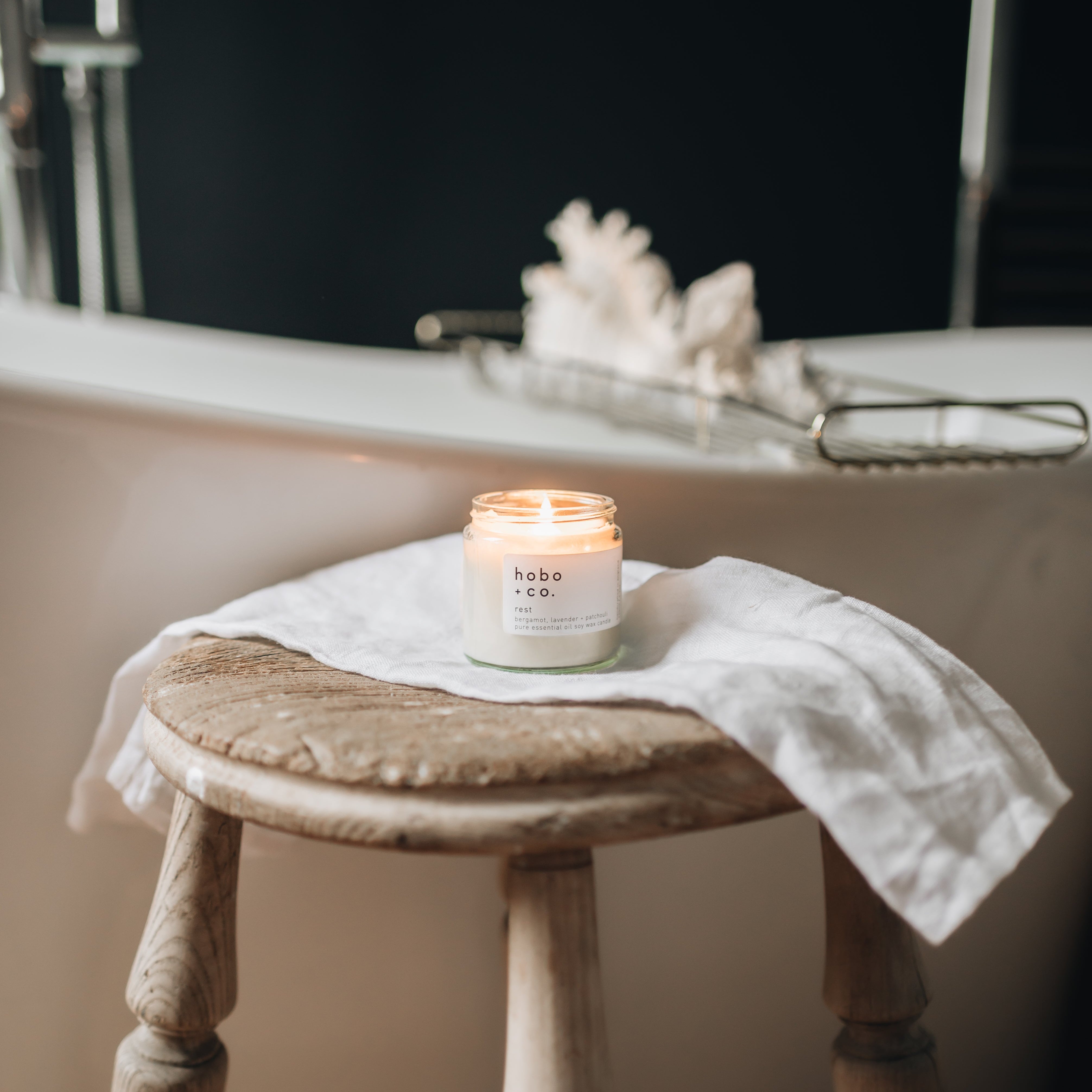 Hobo and co small Candle on a rustic wooden stool in front of a bathtub with a blurred background