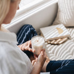 Person holding a lit candle on a couch with a book and blanket