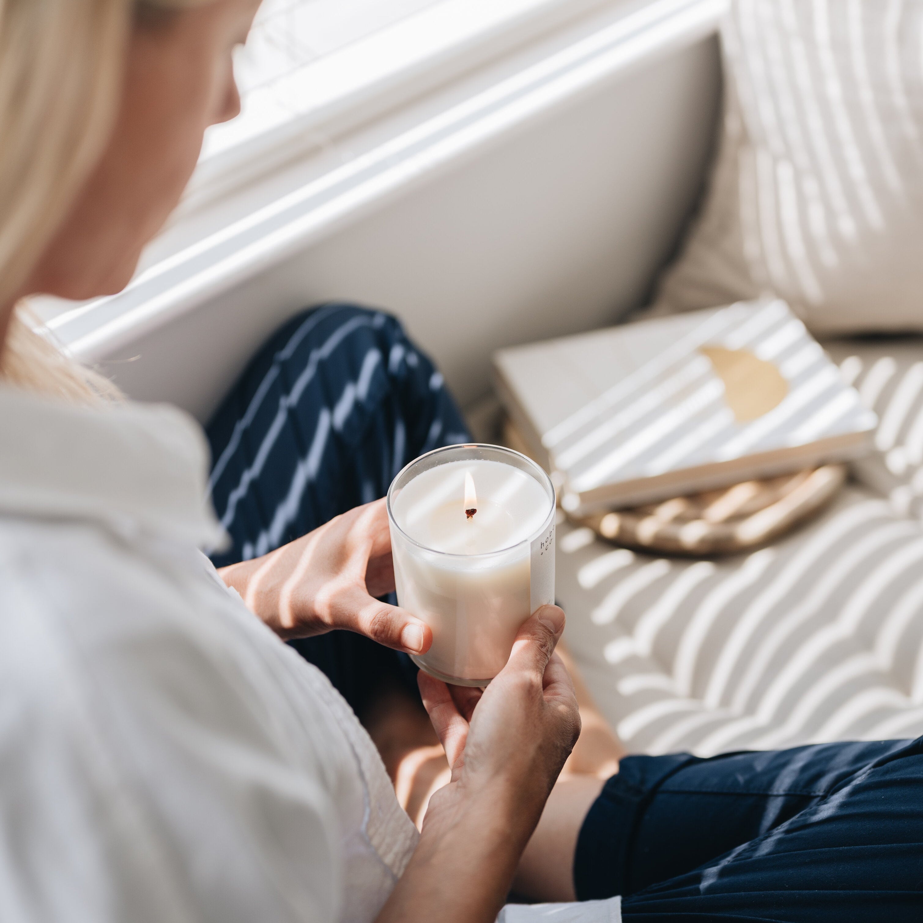 Person holding a lit candle on a couch with a book and blanket