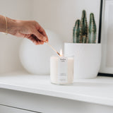 large candle being lit by a match held in a hand on a shelf