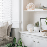 Nook with a window seat, shelves with decor items, a lit candle and plants.