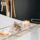 Lit candle with 'hobo' branding on a gold bath tray on a bath with a dark background