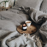 Cozy bedroom scene with a bed, wooden side table, candle, and cup.