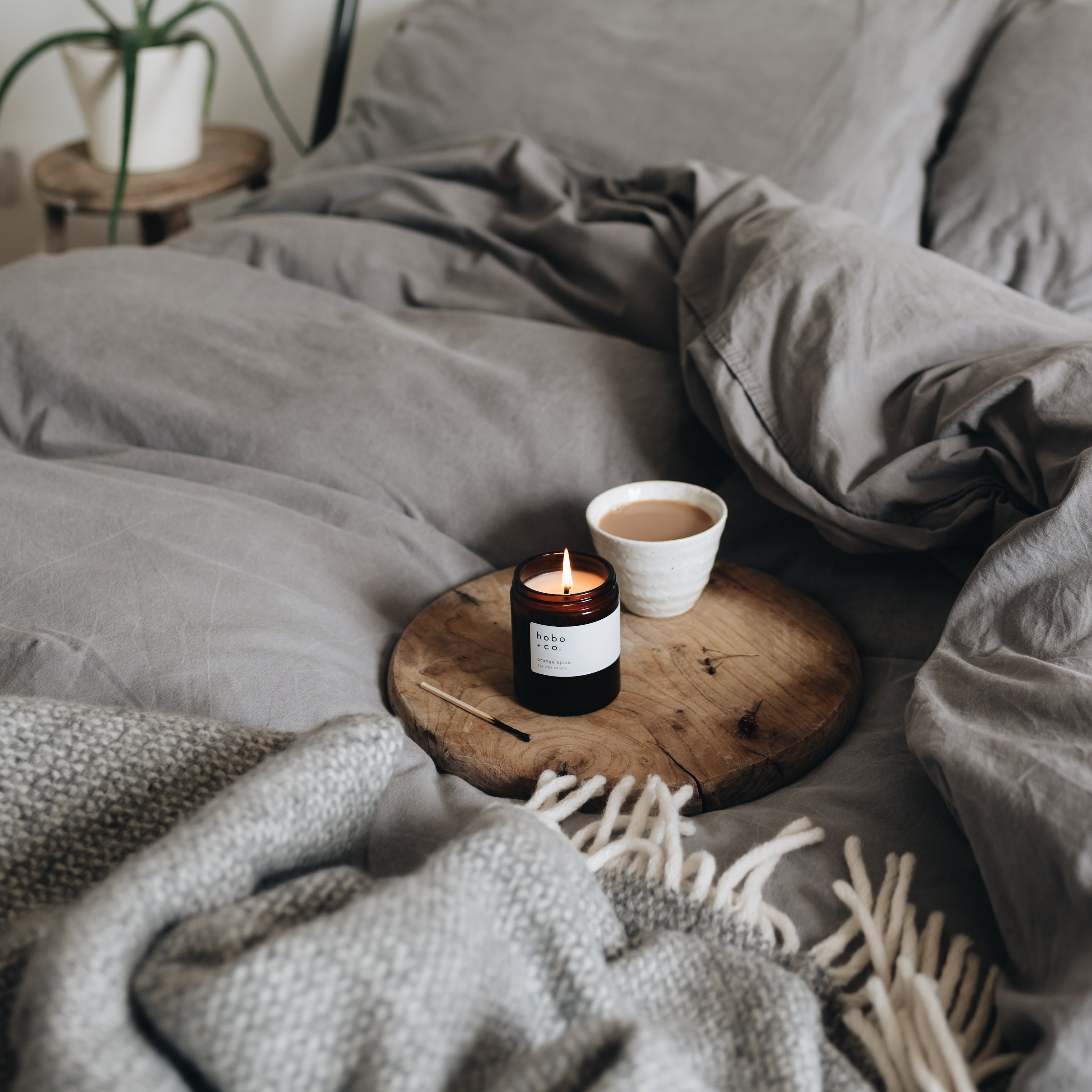 Cozy bedroom scene with a bed, wooden side table, candle, and cup.