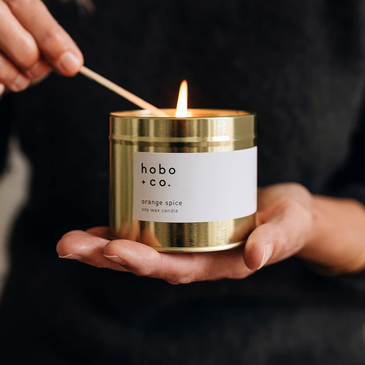 Christmas orange spice festive candle being lit with a match held in hands