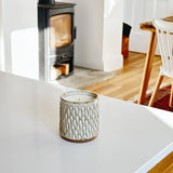 Ceramic candle holder on a white surface with a wood stove in the background.