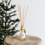 Reed diffuser with 'hobo + co' label on a wooden surface with a blurred Christmas tree in the background.
