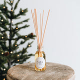 Reed diffuser with 'hobo + co' label on a wooden surface with a blurred Christmas tree in the background.