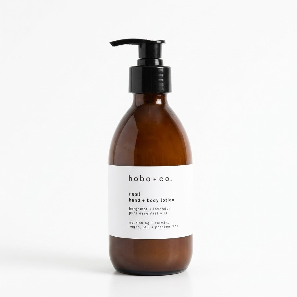An amber glass pump bottle of hobo + co. rest hand and body lotion with a white label and black pump, set against a clean white background.