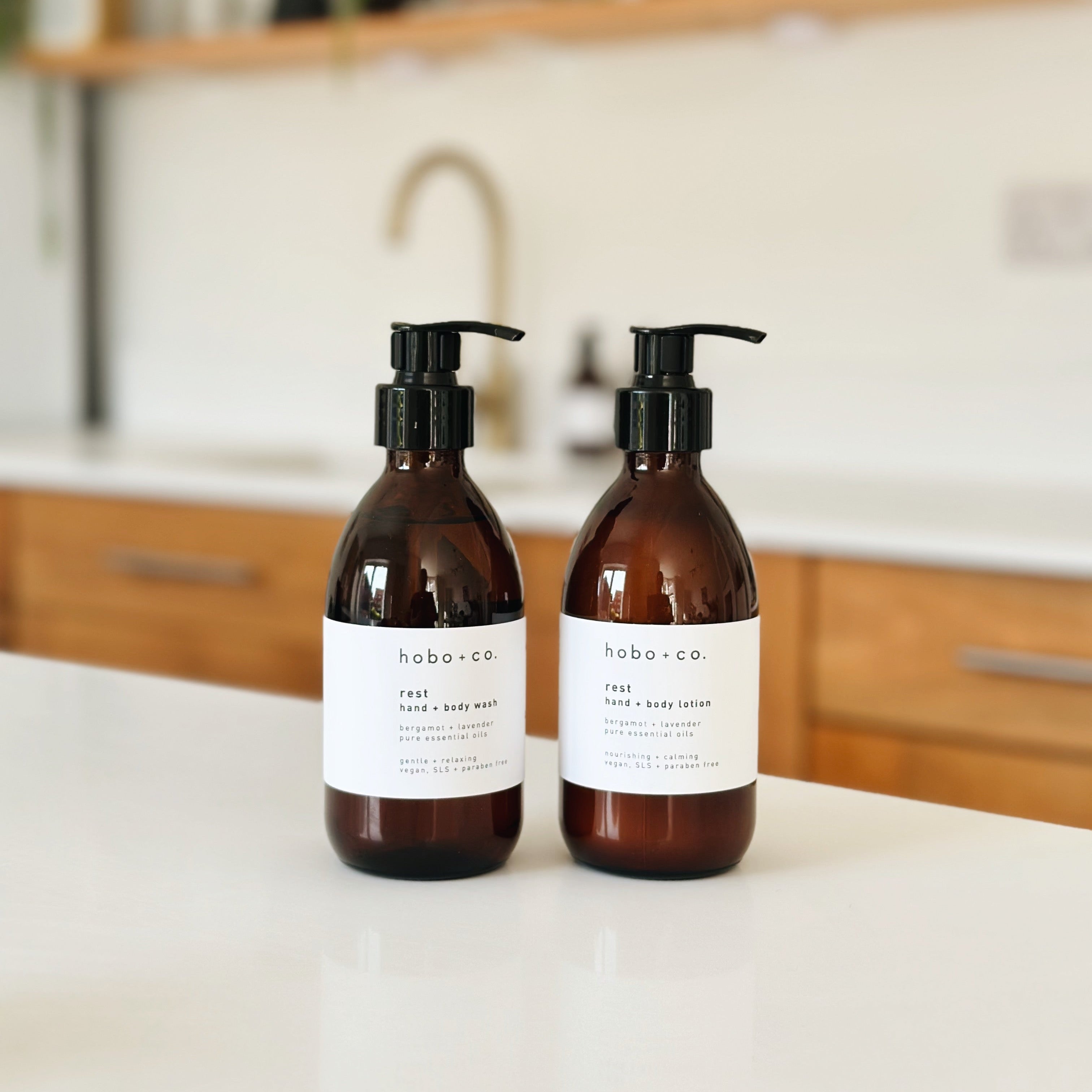 Two amber glass pump bottles of hobo and co body wash on a white countertop in a bright kitchen setting.
