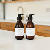 Two amber glass pump bottles of habo.co body wash on a white countertop in a bright kitchen setting.