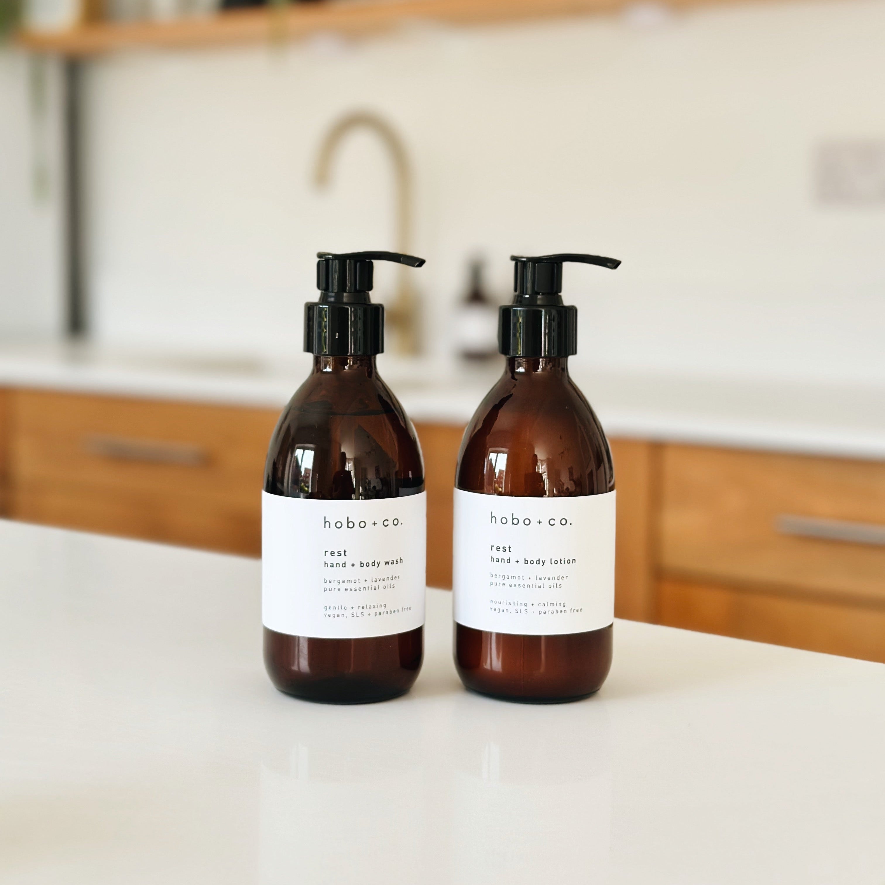 Two amber glass pump bottles of habo.co body wash on a white countertop in a bright kitchen setting.