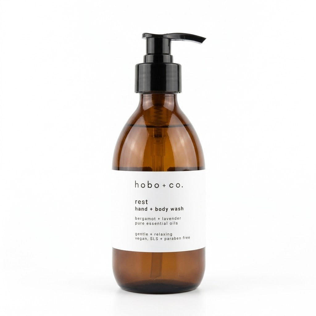 An amber glass pump bottle of hobo + co. hand and body wash with a white label and black pump dispenser, set against a plain white background.