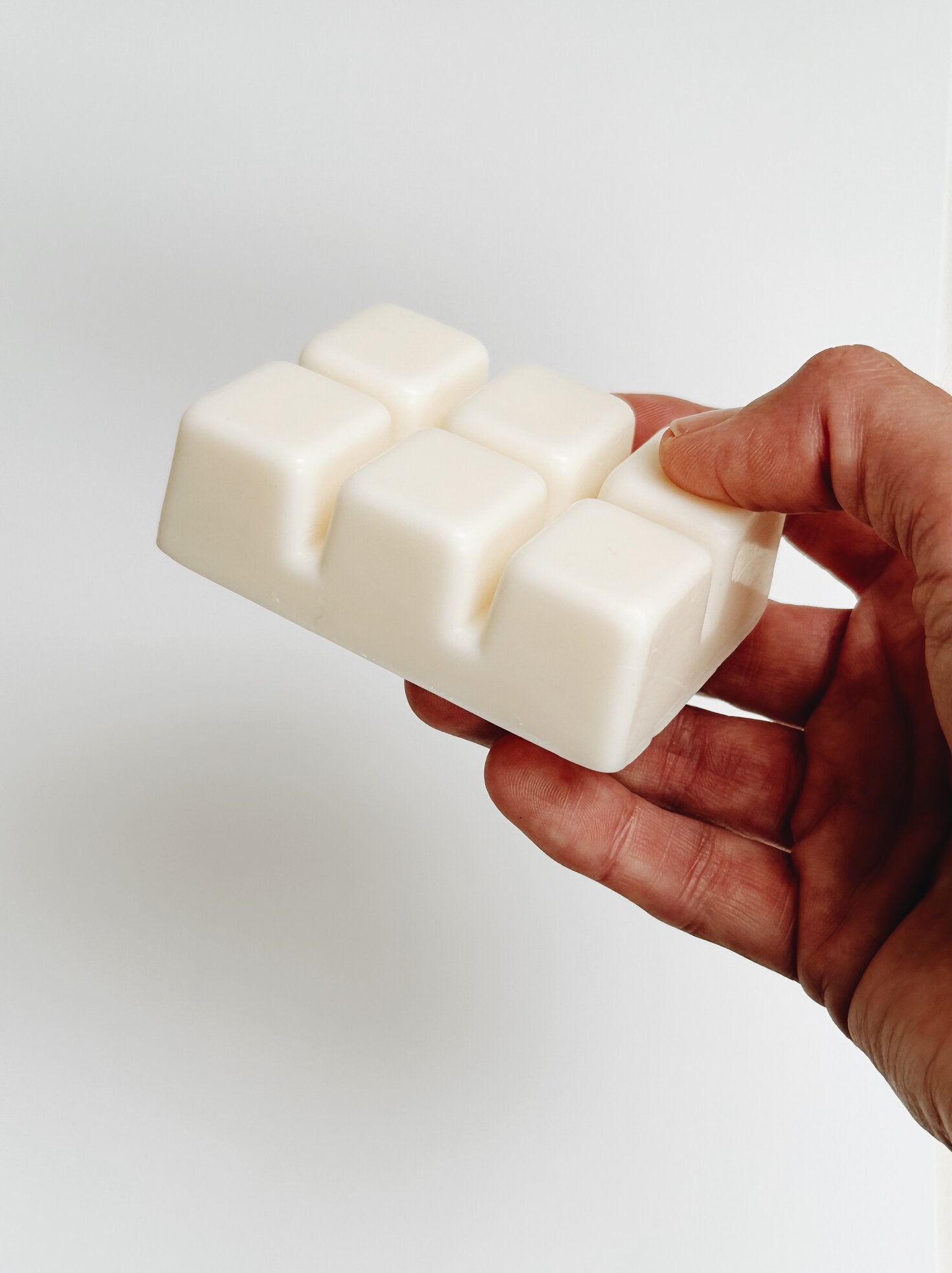 Hand holding a shobo + co soy wax melt bar against a light gray background