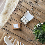 Rustic wooden table with a box of white festive tealights and a plant on a wooden floor with a cosy sheepskin rug.