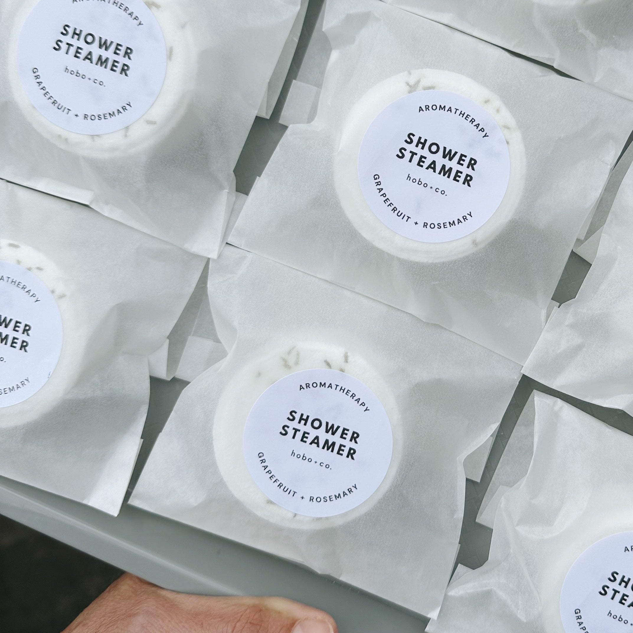 Multiple shower steamers in packaging with a hand holding the tray. Eco-friendly handmade shower steamer gift