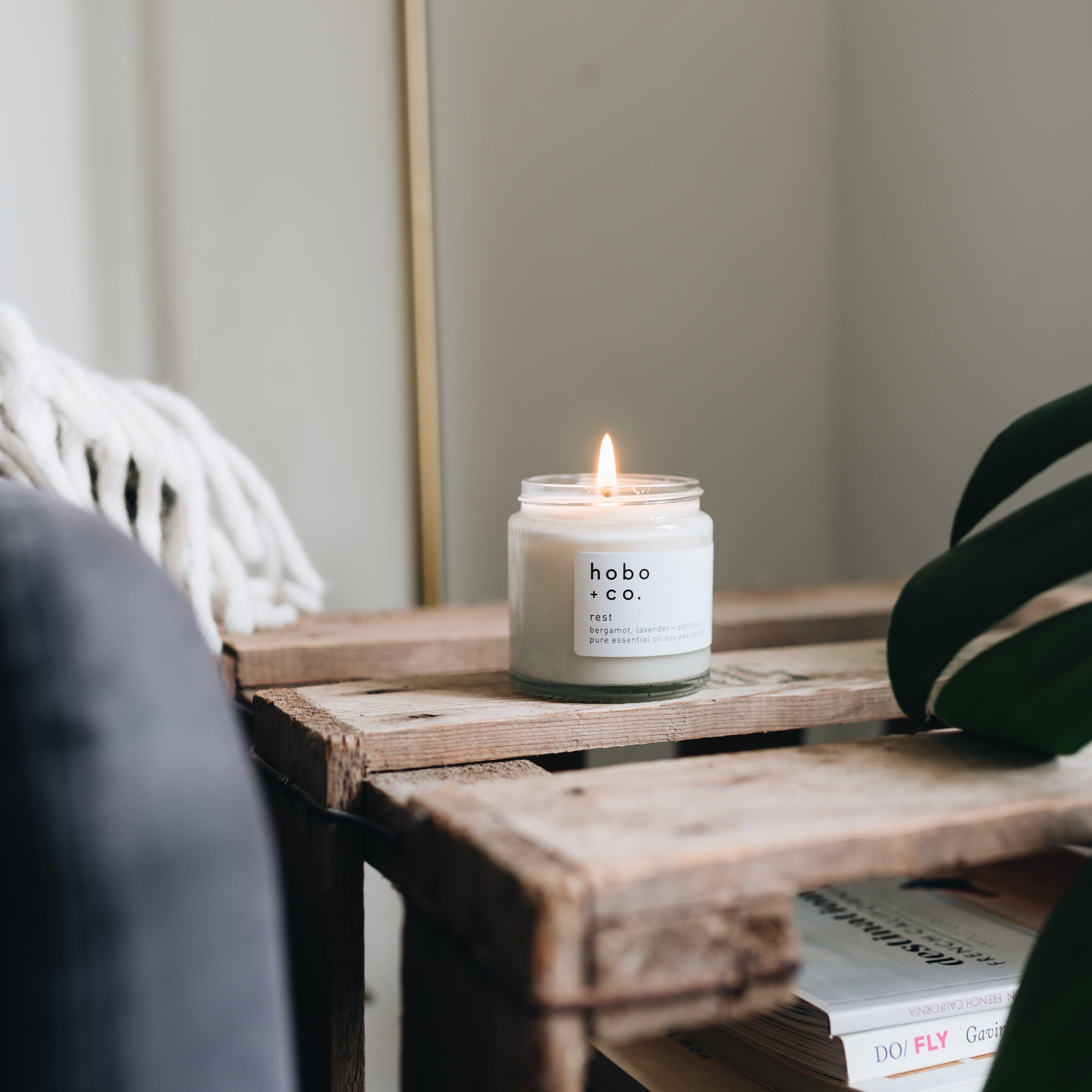Hobo and co Candle on a wooden side table with books and a plant in a blurred indoor setting