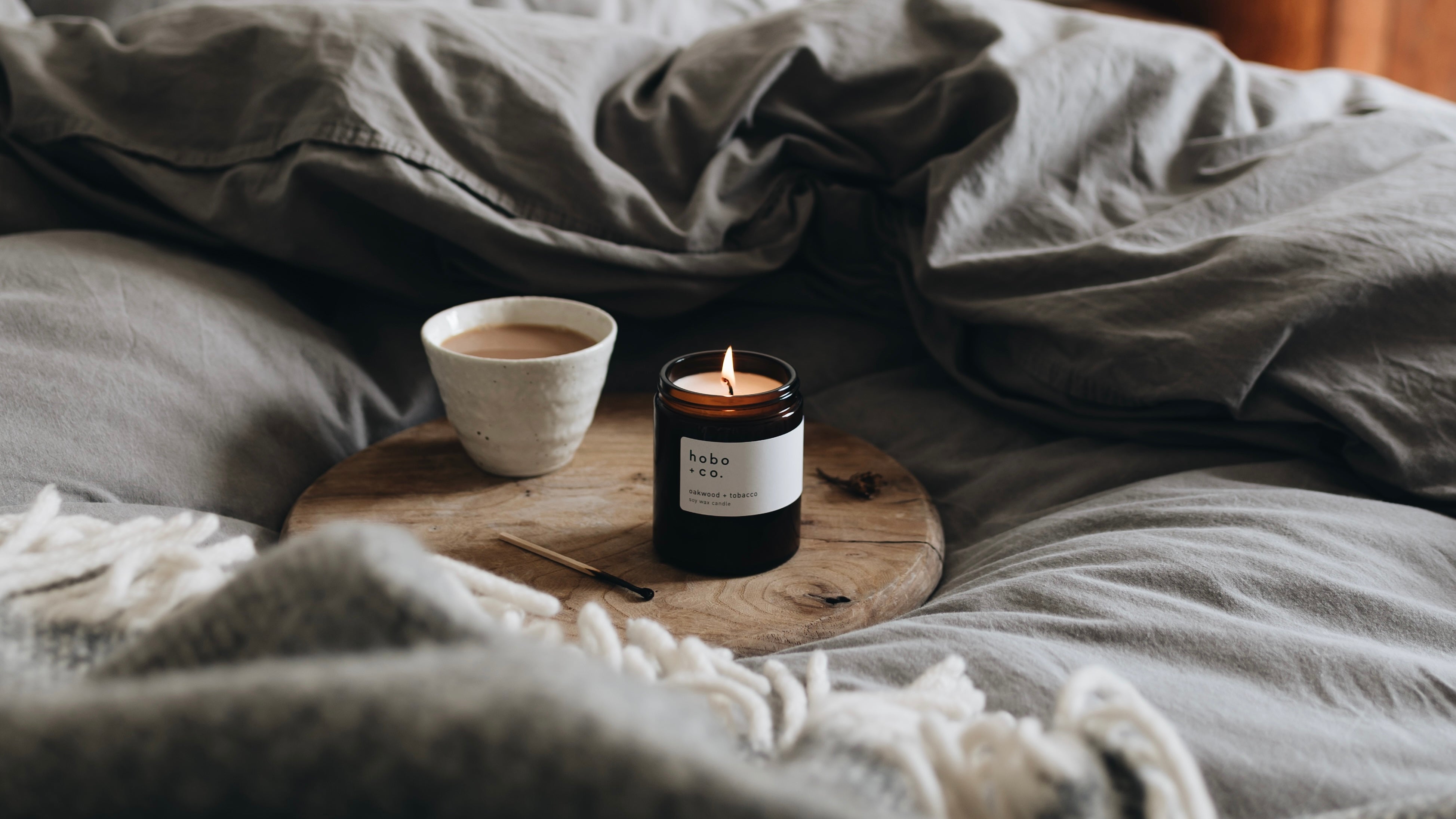 Oakwood and tobaacco medium jar candle  which is lit in a cosy bedroom  
